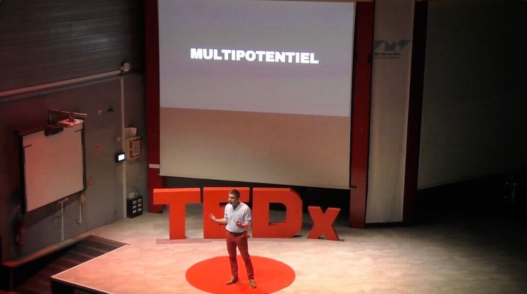 Julien Tedx multipotentiel Orateur (Julien De Lopez) sur scène TEDx expliquant la définition du profil multipotentiel avec écriture sur écran géant.